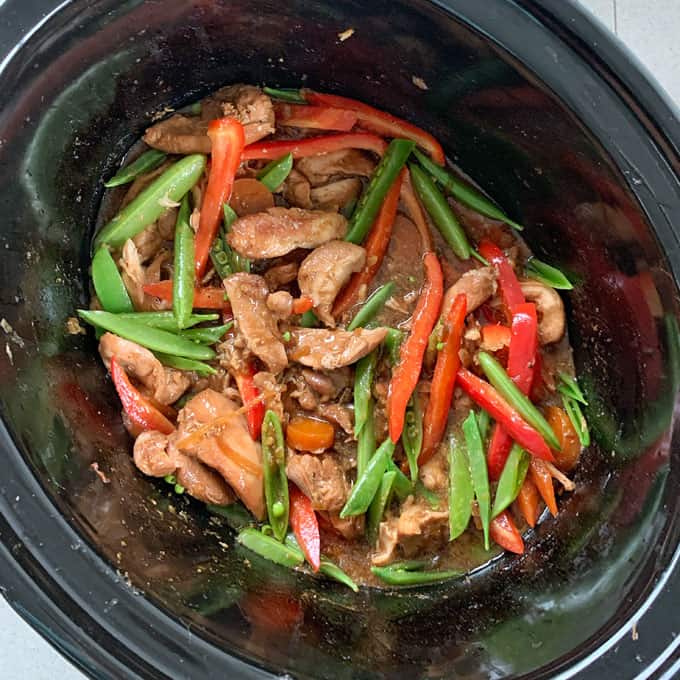 Sliced chicken, red bell peppers, and snap peas are combined for a flavorful Slow Cooker Honey Soy Chicken dish, ready to be cooked with sauce.