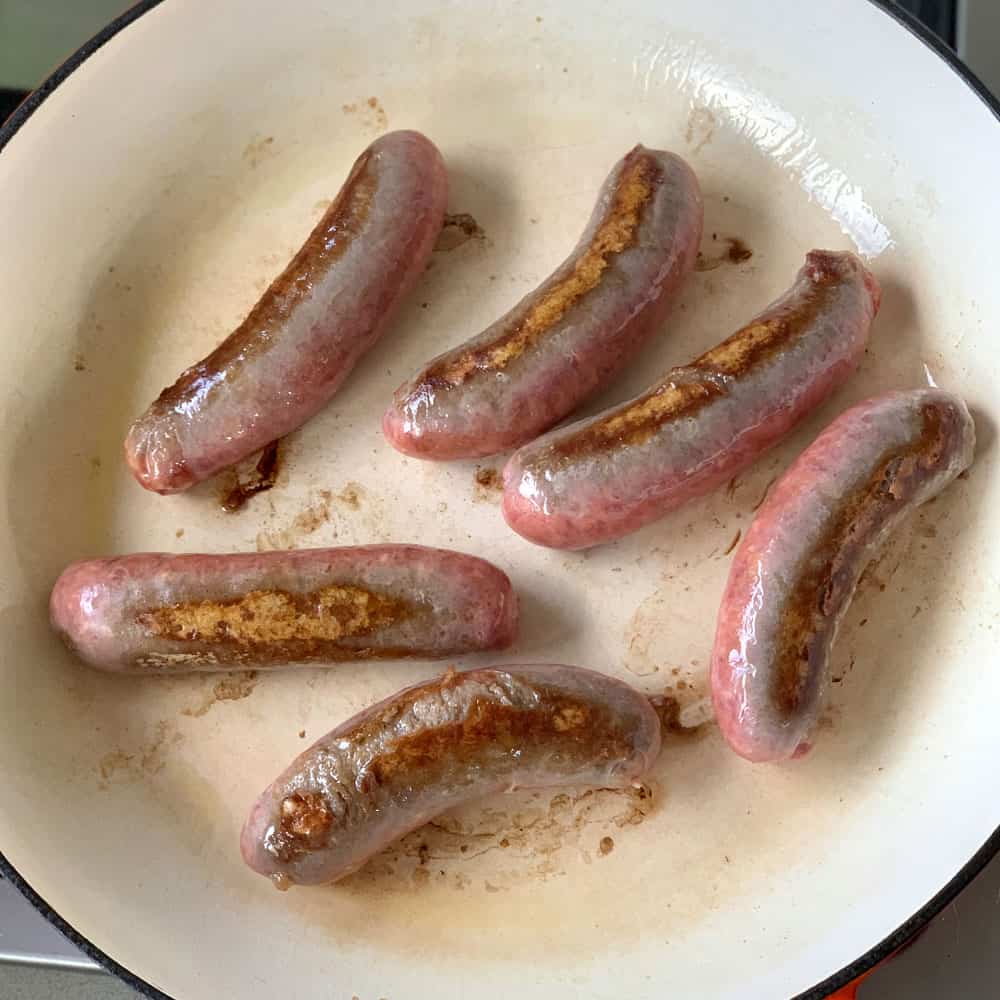 Sausages cooking a cast iron dish.