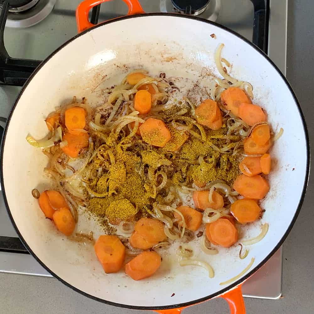 Carrots, onions and curry powder in a cast iron dish.