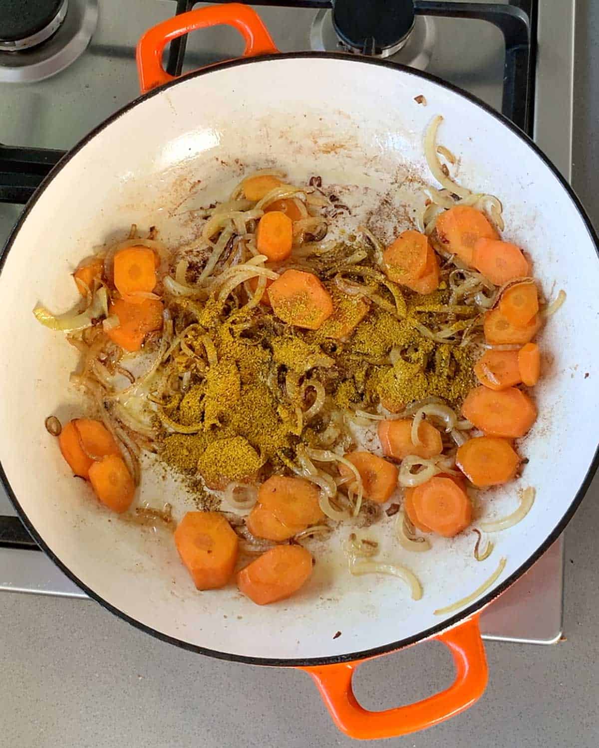 Onions, carrots and curry powder cooking in a cast iron dish.