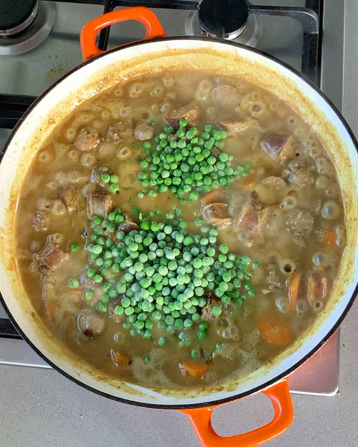 Curried sausages and peas cooking in a casserole dish.