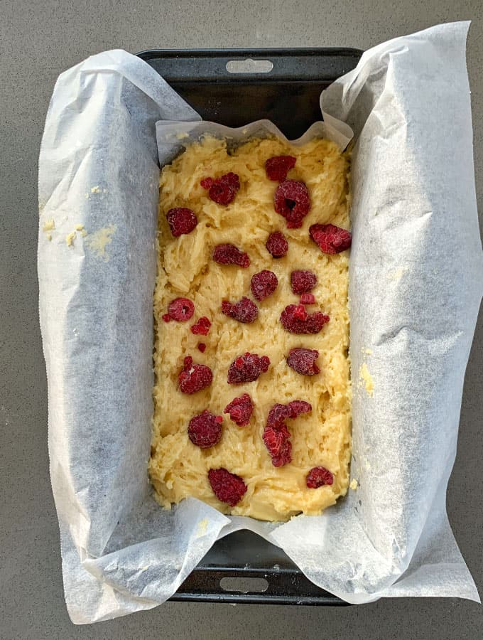 Raspberry and Lemon Loaf A rectangular baking pan lined with parchment paper contains unbaked Raspberry and Lemon Loaf batter, topped with scattered raspberries.