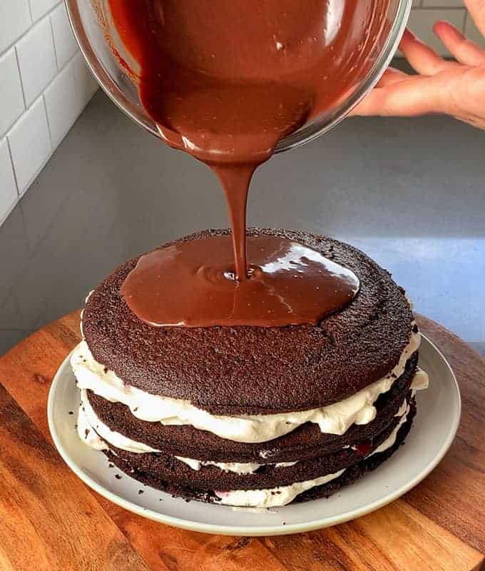 A luscious chocolate ganache cascades over a layered Black Forest Gateau, elegantly resting on a pristine white plate.
