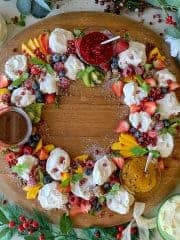 Birds eye view of a mini pavlova wreath with dipping suace sitting on a large wooden circular board.