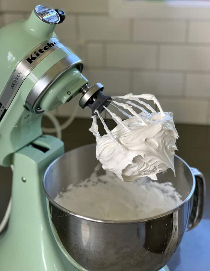 a mint kitchen aid mixer on a bench with whisked egg white on the whisk attachment.