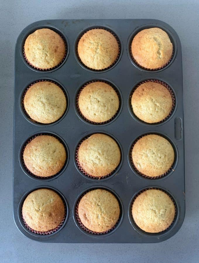 A muffin tin containing twelve freshly baked banana muffins rests on a gray countertop.