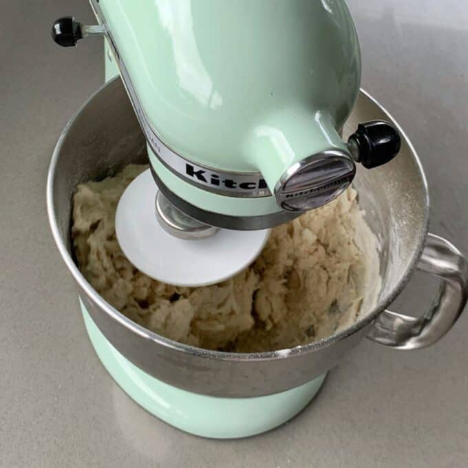 Pizza dough being mixed on a green Kitchen Aid mixer on a grey bench.