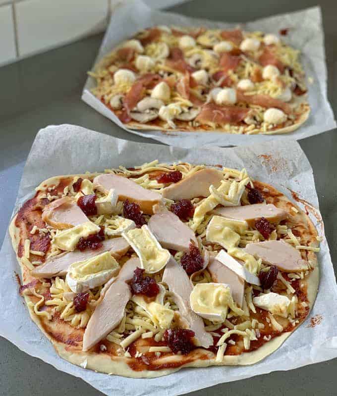 2 chicken cranberry pizzas sitting on a wooden chopping board.