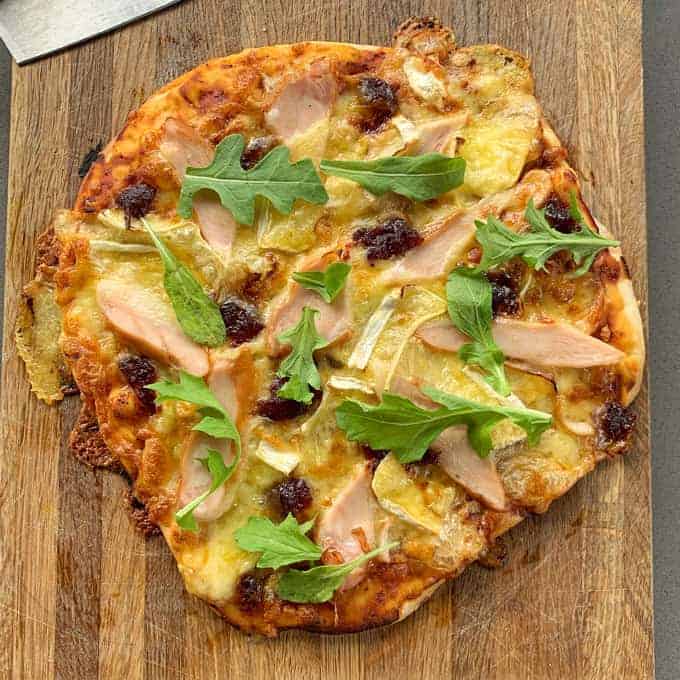 A cooked chicken cranberry pizza on a wooden chopping board.