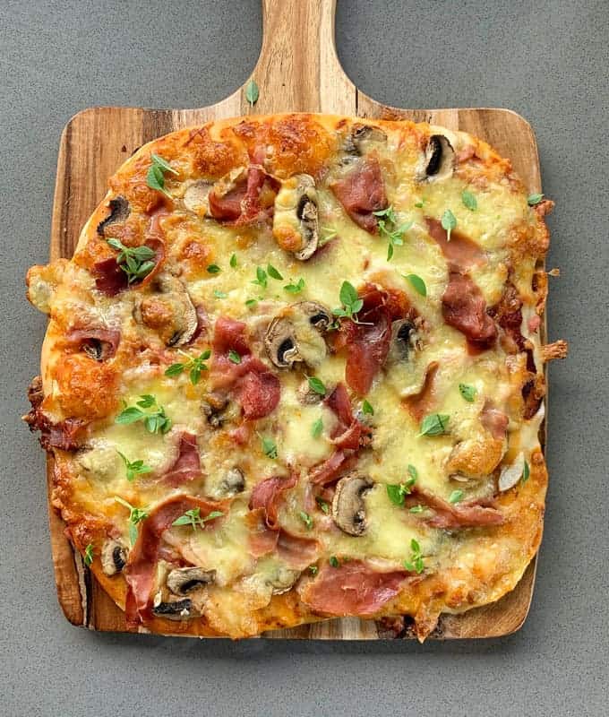 A cooked mushroom and prosciutto pizza on a wooden chopping board.