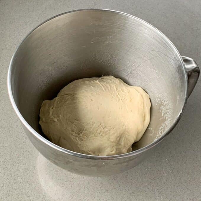 Pizza dough sitting in the bowl of a stand mixer.