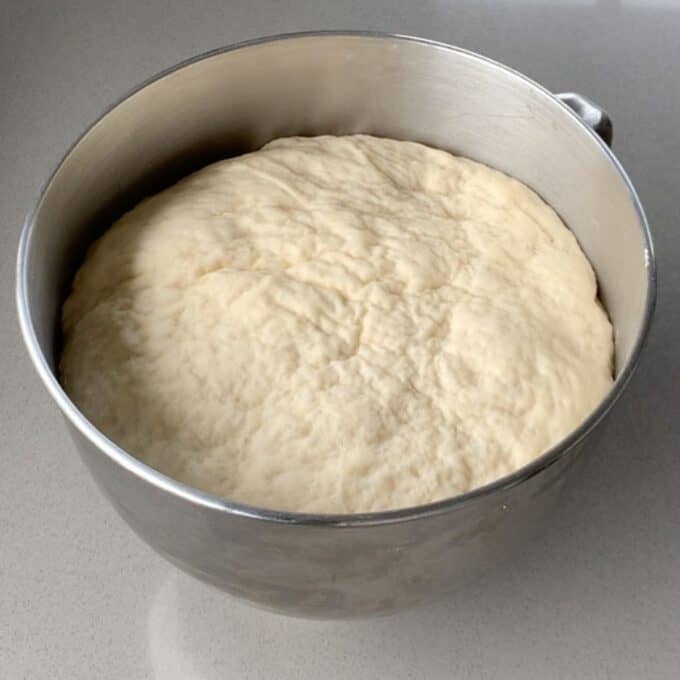 Risen pizza dough sitting in the bowl of a stand mixer.