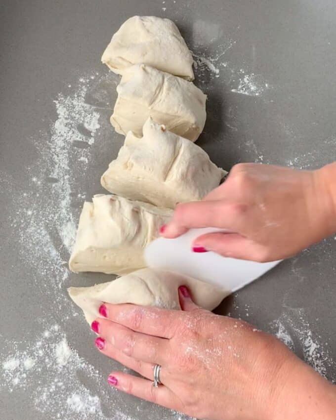 Pizza dough being cut into 5 equal portions on a grey bench top.