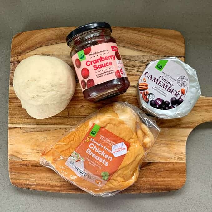 The ingredients to make a chicken cranberry pizza on a wooden chopping board