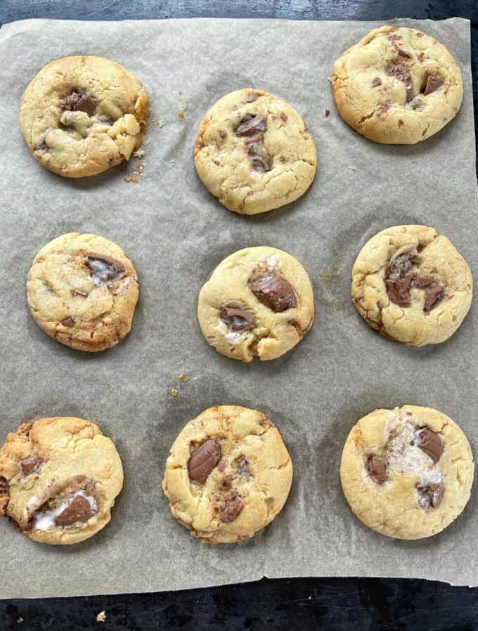 Nine freshly baked Creme Egg Cookies with chocolate chunks sit enticingly on a parchment-lined baking sheet.