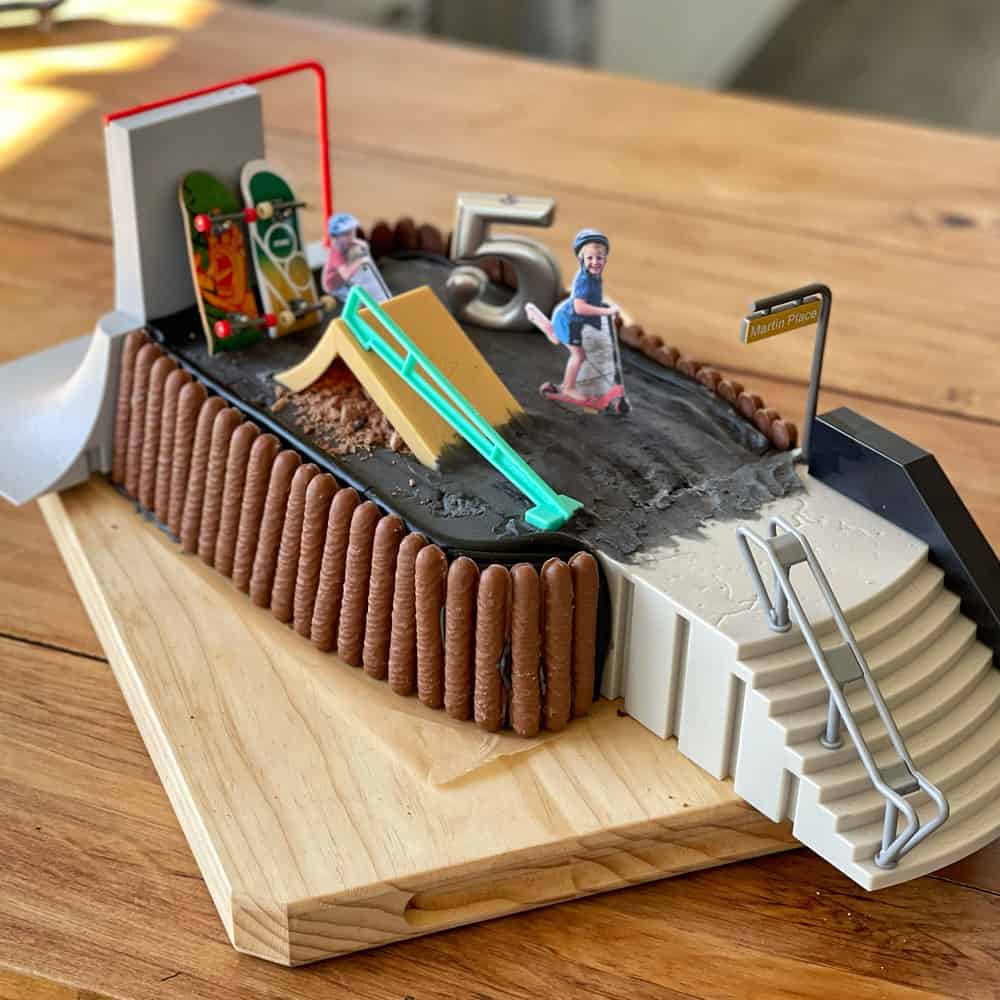 A birthday cake decorated to look like a skate park sitting on a wooden board.