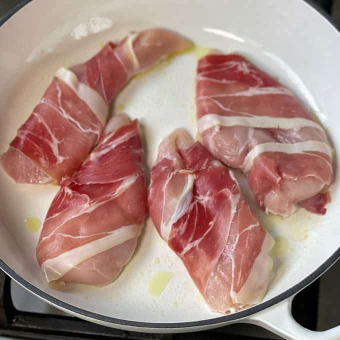 Four pieces of raw chicken wrapped in prosciutto are placed in a white skillet with a small amount of oil, the perfect start for a flavorful one pot chicken and gnocchi meal ready to be cooked.