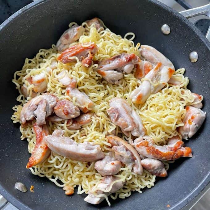 A black frying pan containing cooked Chicken Satay Noodle Stir Fry, with tender noodles and pieces of browned chicken.