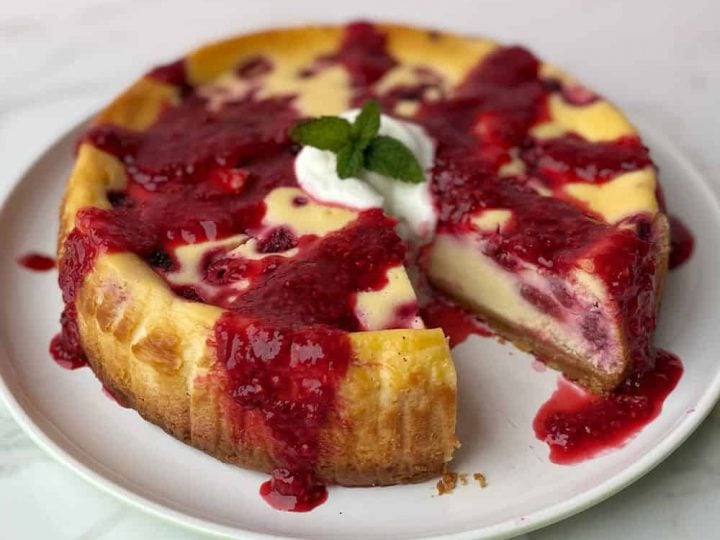 A close up of a baked raspberry cheesecake on a white plate.