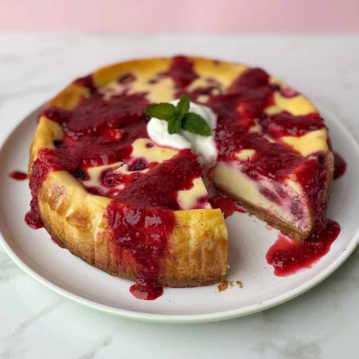 A close up of a baked raspberry cheesecake on a white plate.