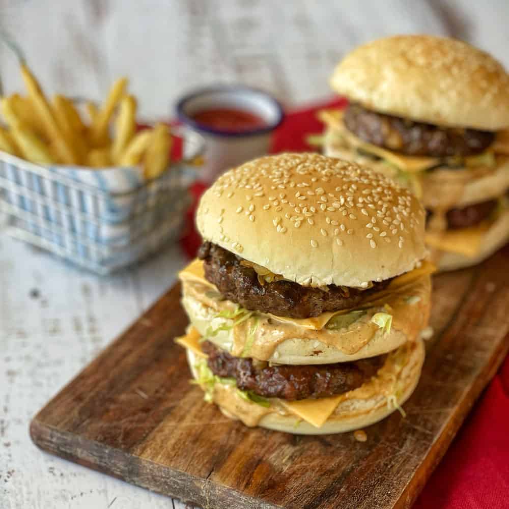 A close up of a big mac style burger on a wooden board.