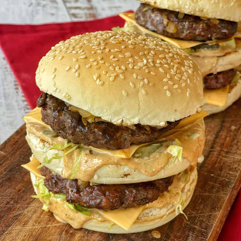 A close up of a big mac style burger on a wooden board.