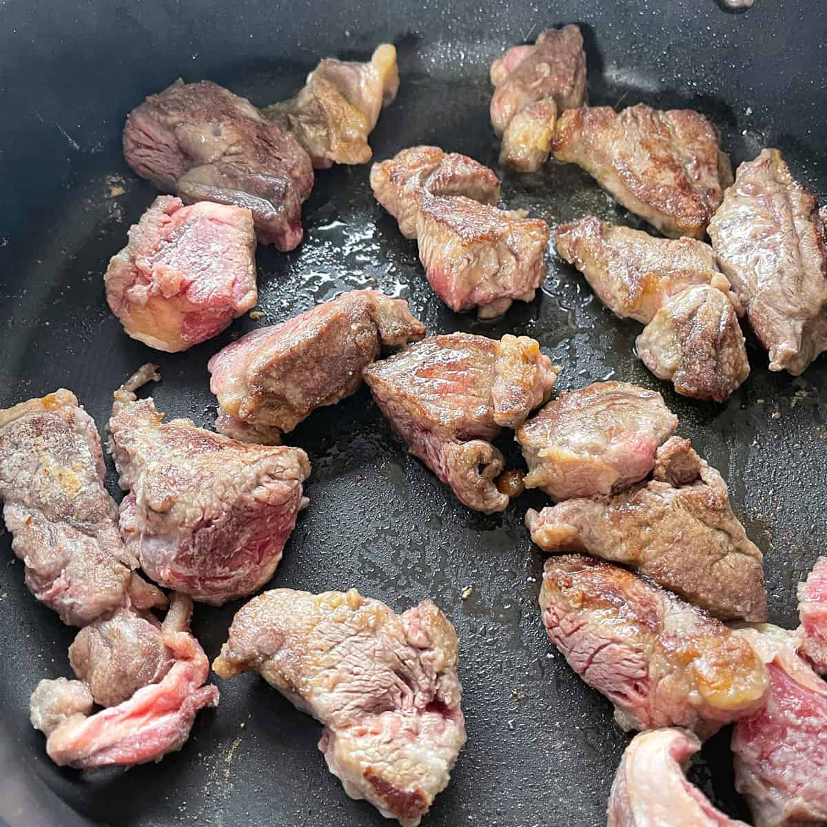 Close up of beef cooking in a black frying pan.