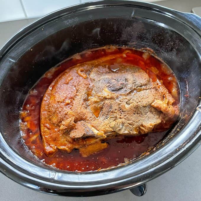 Slow Cooker Mexican Pulled Pork A seasoned Slow Cooker Mexican Pulled Pork roast simmers in a slow cooker, surrounded by rich red sauce and flavorful juices.