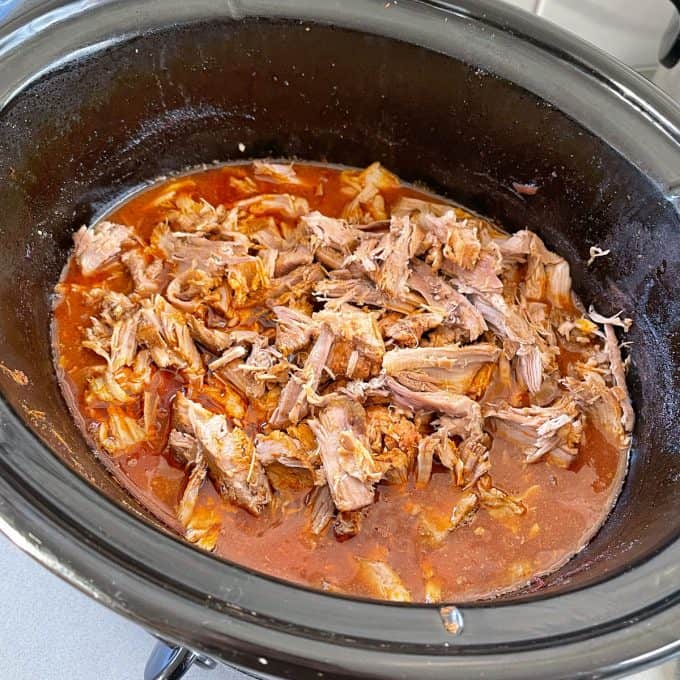 Slow Cooker Mexican Pulled Pork Slow Cooker Mexican Pulled Pork simmers as shredded cooked meat in a rich red sauce inside a black slow cooker.