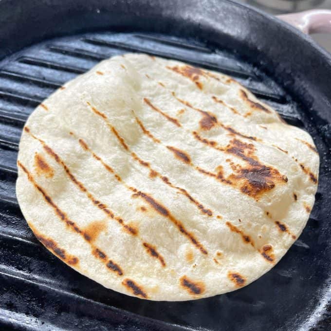 A flour tortilla with grill marks cooking on a black grill pan, perfect for wrapping up slow cooker Mexican pulled pork.