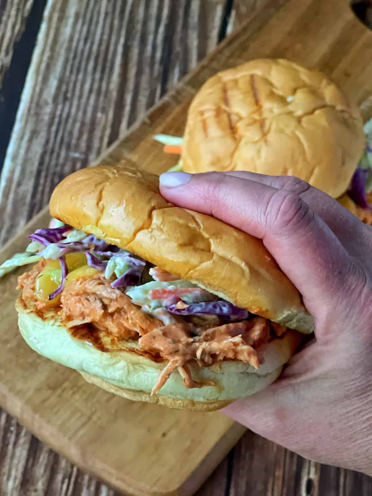 A hand holding a burger with shredded chicken and coleslaw.