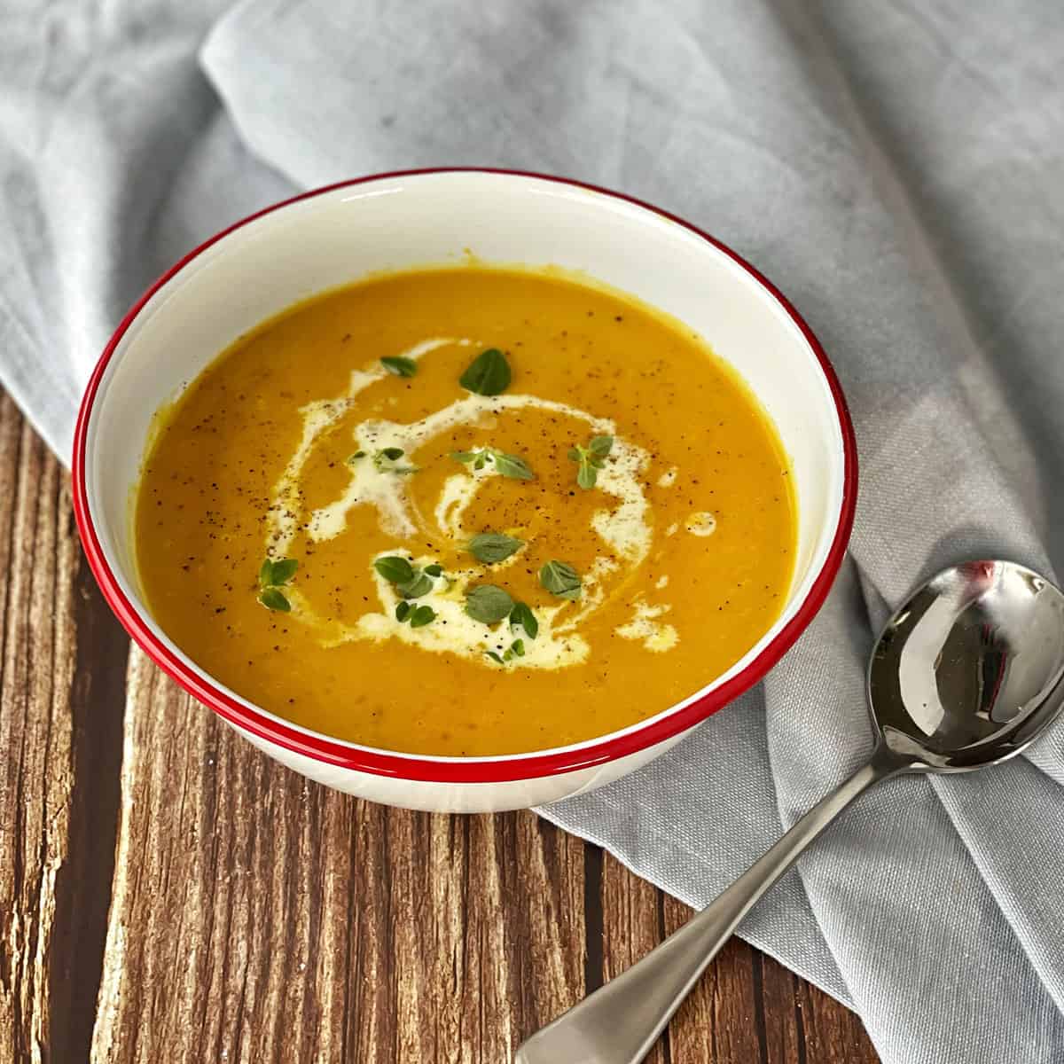 Pumpkin soup in a white bowl on a wooden bench.