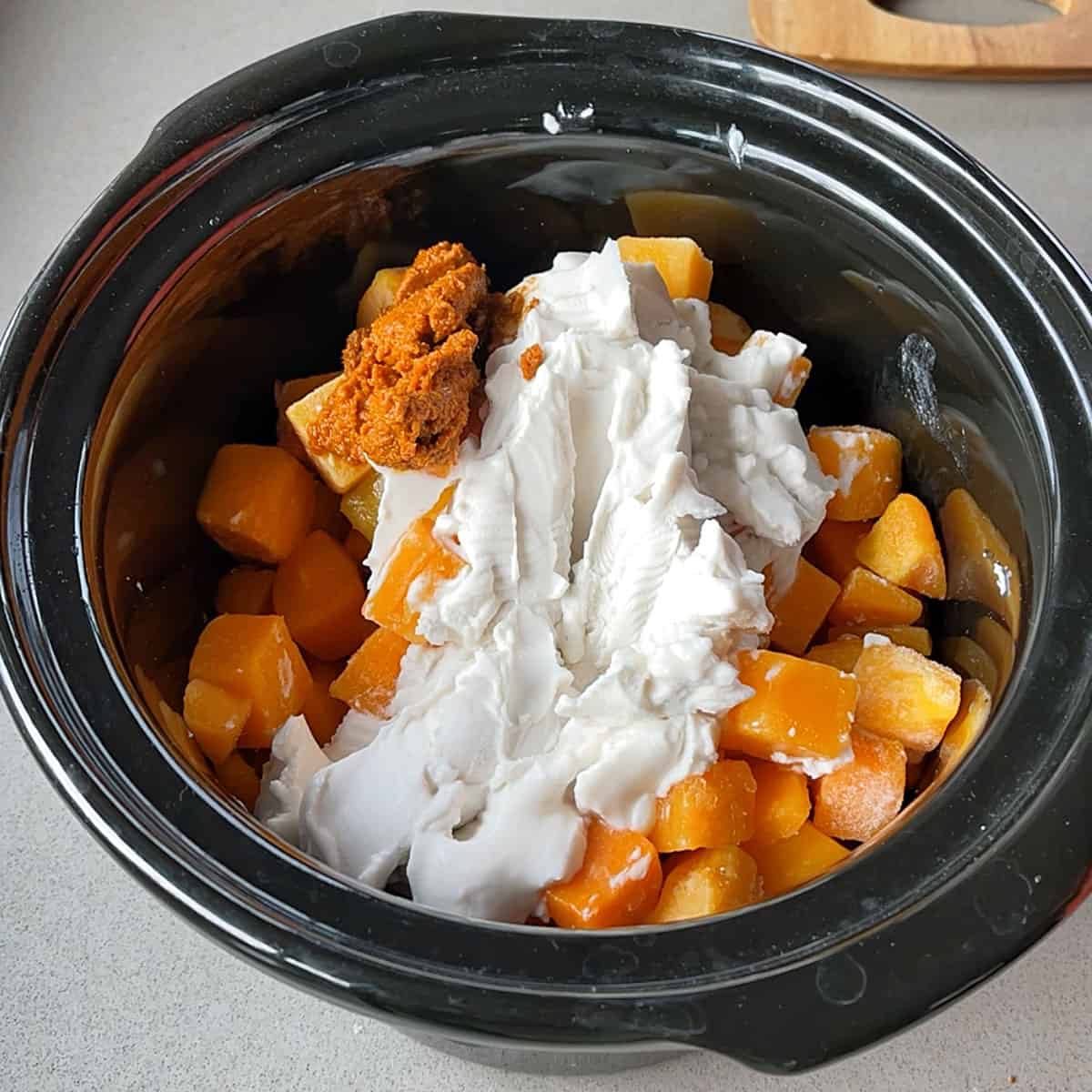 Pumpkin soup ingredients in a black slow cooker.