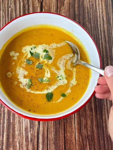 Pumpkin Soup in a white bowl on a wooden bench.
