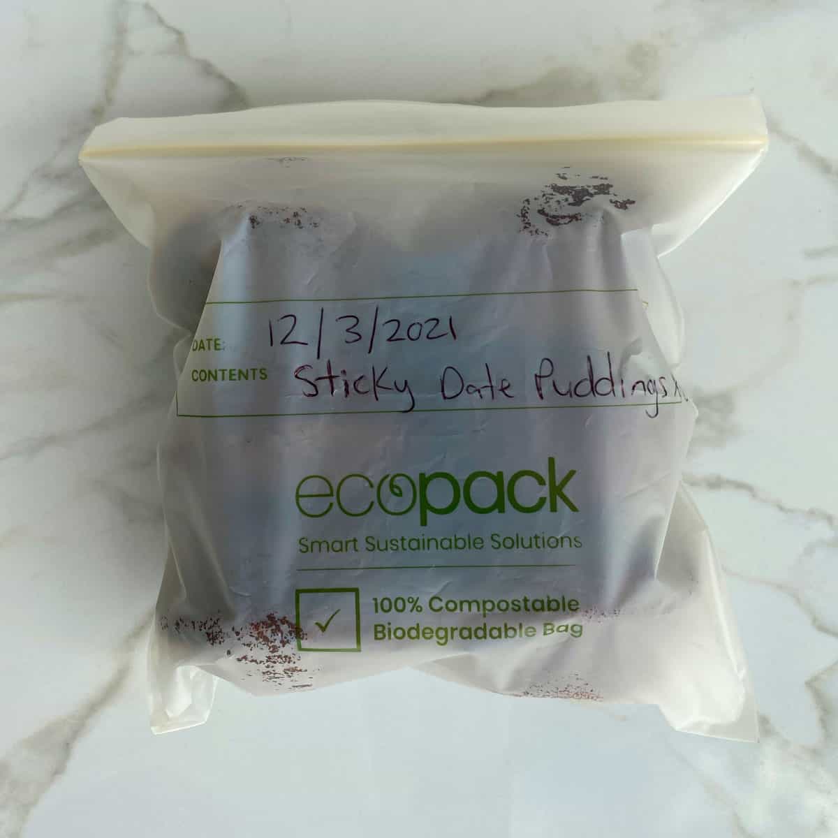 Mini sticky date puddings in a freezer bag on a white bench.