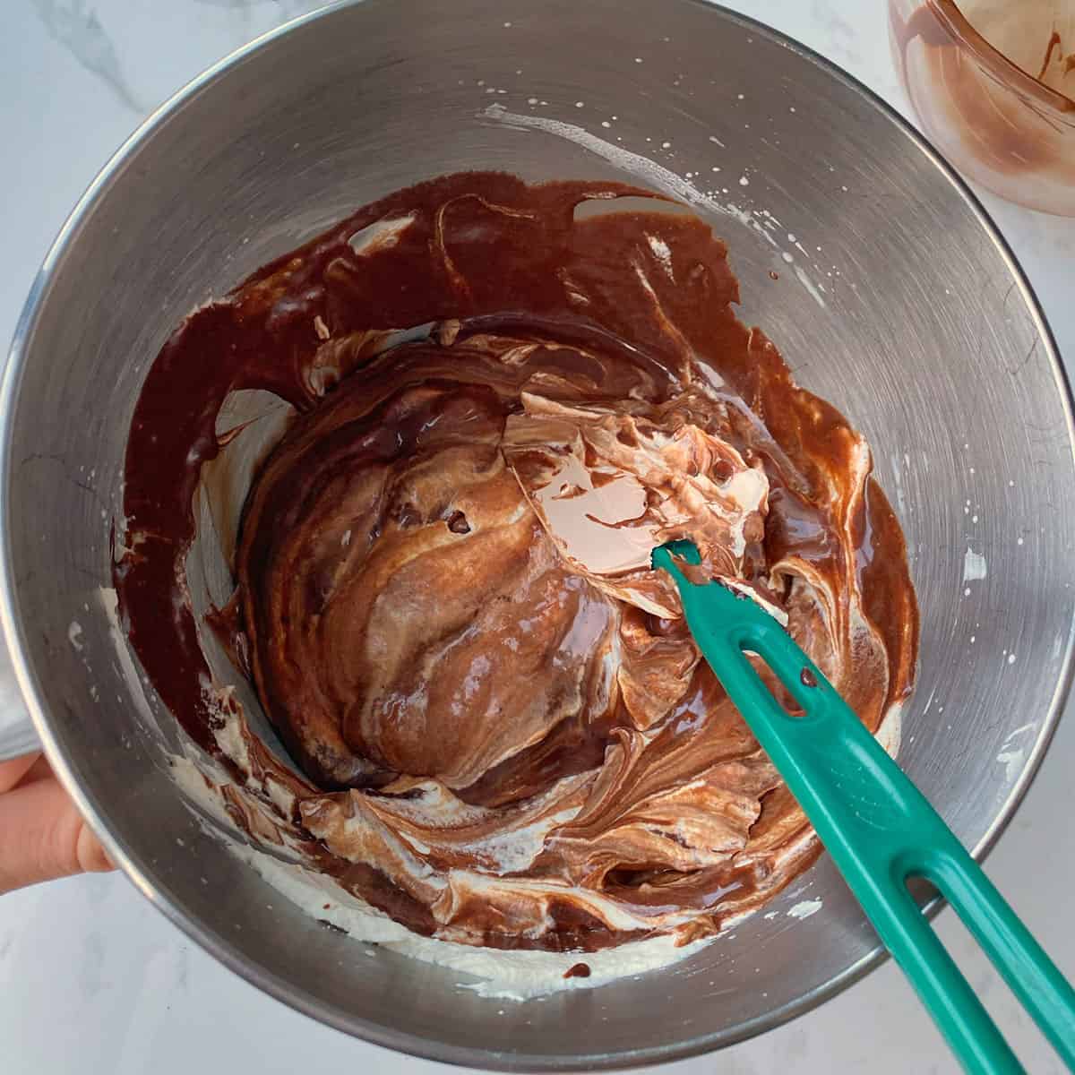 Whipped cream being folded into melted chocolate in a pot with a spatula.