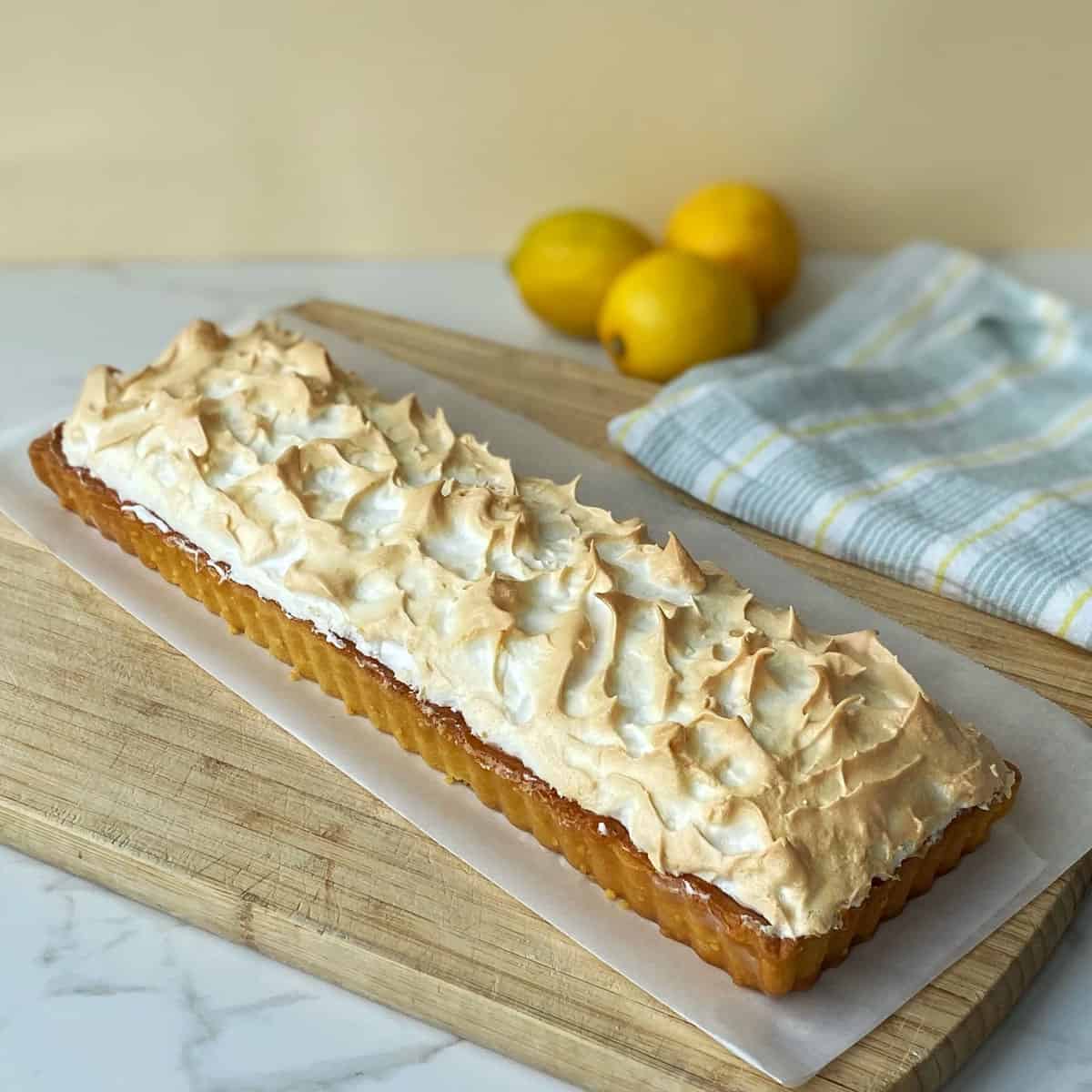 A baked, whole Lemon Meringue Pie on a wooden chopping board.