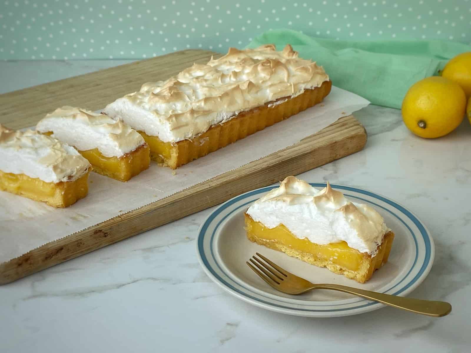 Slices of Lemon Meringue Pie on a chopping board and a white plate.