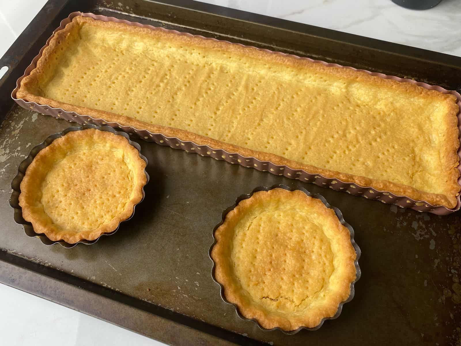 A large rectangle tin and two small round tins with baked pastry in them.