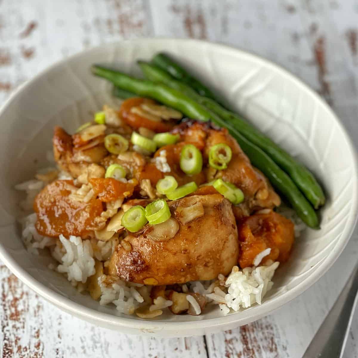 Apricot chicken served with rice and beans in a white bowl.