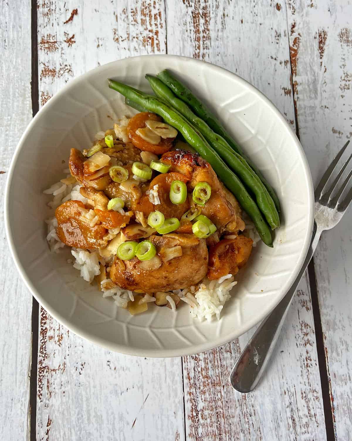 Apricot chicken served on rice with green beans in a white bowl.