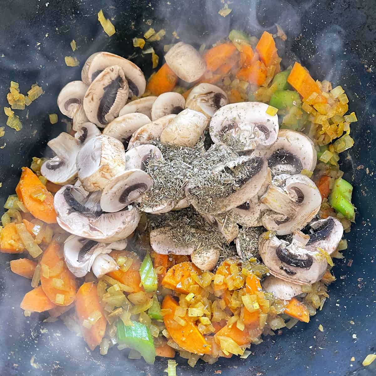 Vegetables, mushrooms and herbs cooking in a pot.