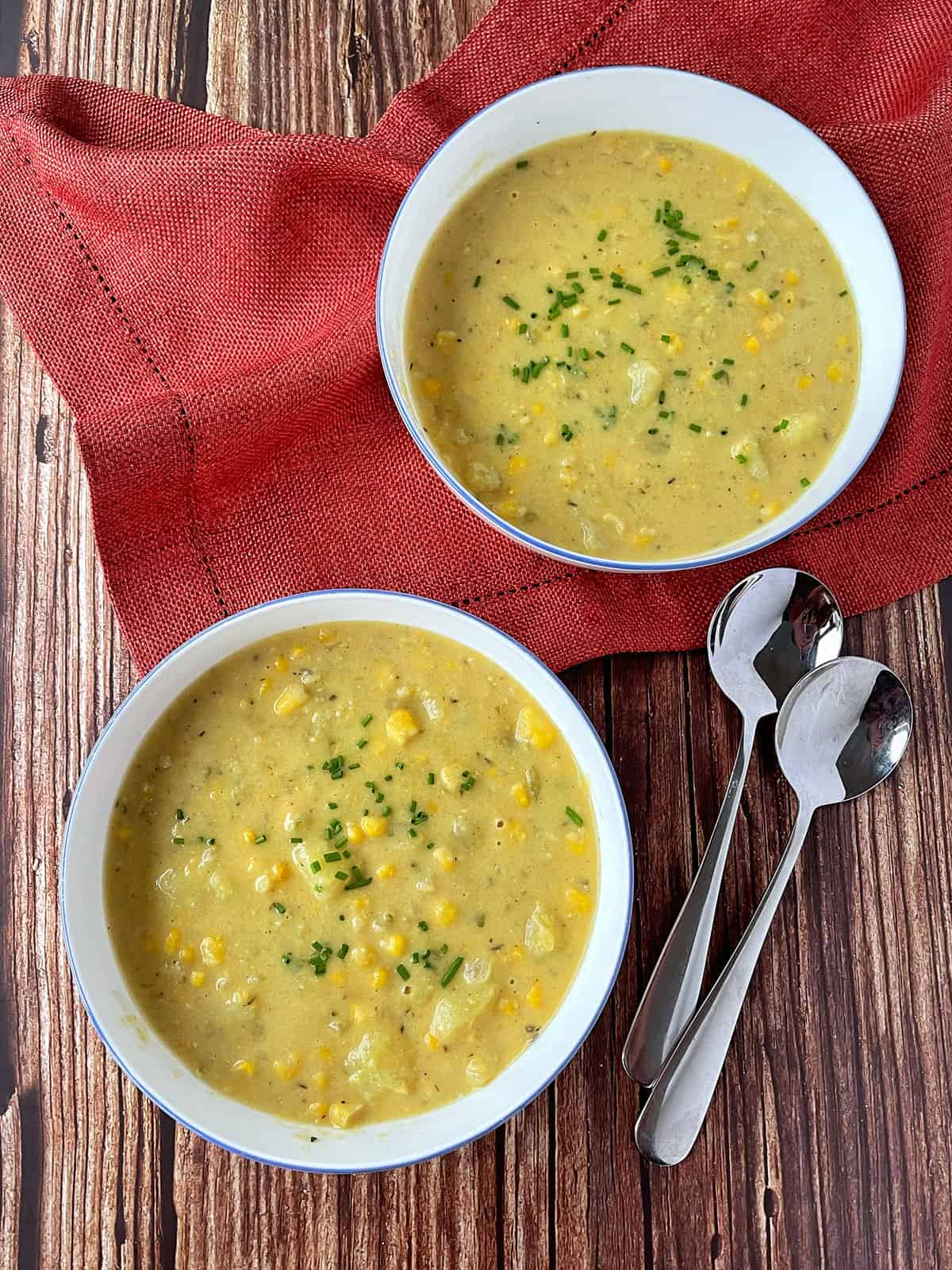 Two white bowls of corn and potato chowder on a wooden table