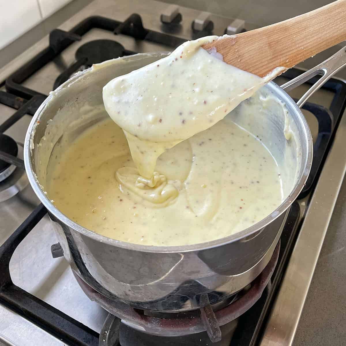 A wooden spoon in a pot with cheese sauce.