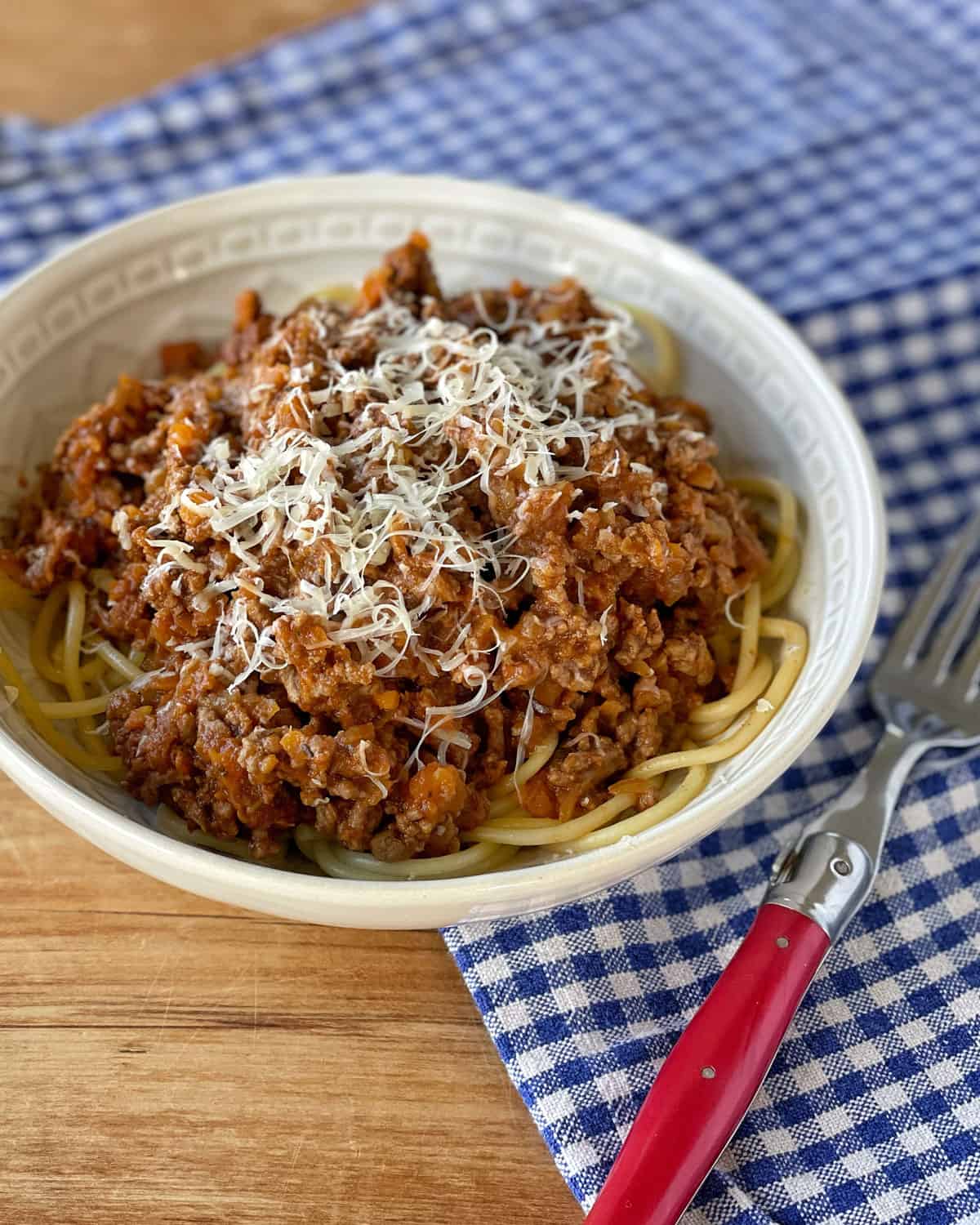 Spaghetti Bolognese in a white bowl on a checked tablecloth.
