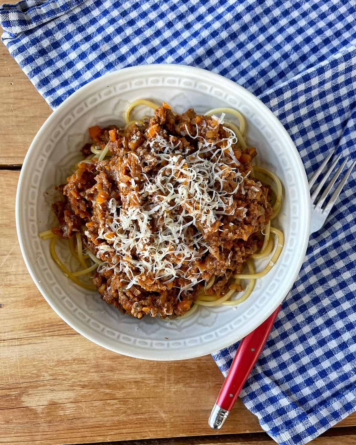 Spaghetti Bolognese in a white bowl sitting on a checked tablecloth.