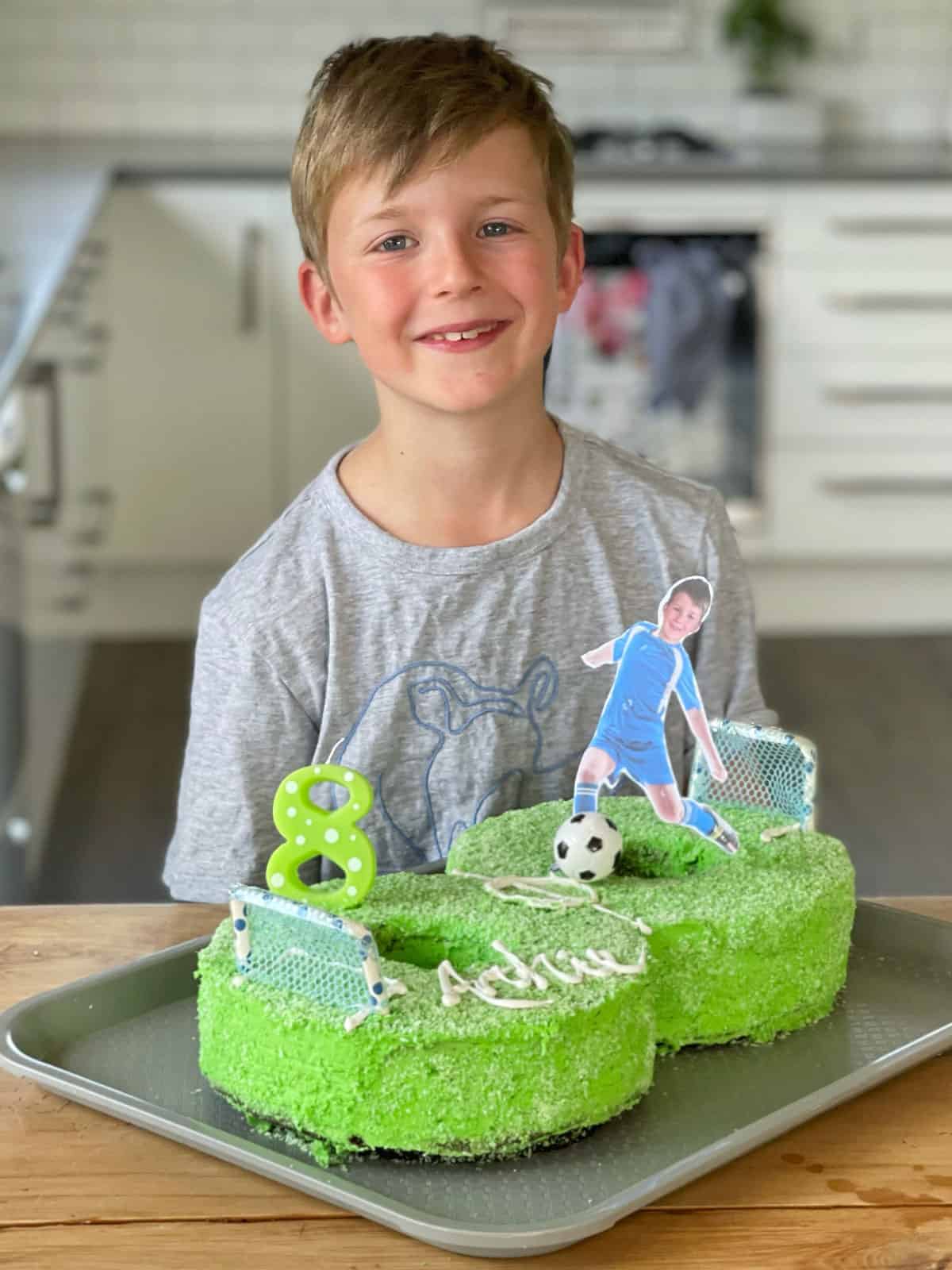 A boy standing behind his number 8, football themed birthday cake.