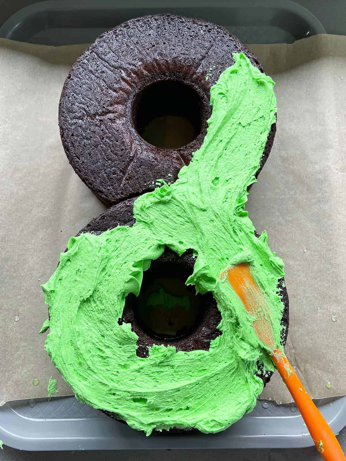 A chocolate cake being iced with green buttercream icing.