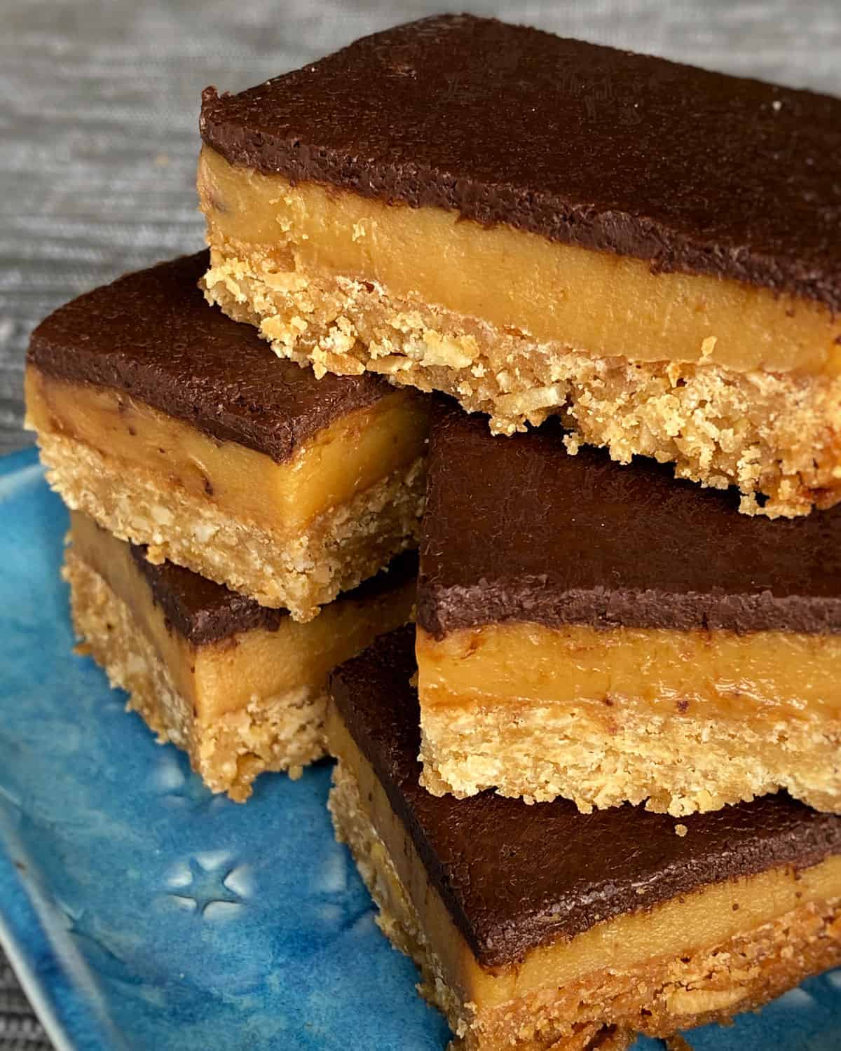 A close up of Caramel coconut slice on a blue plate.