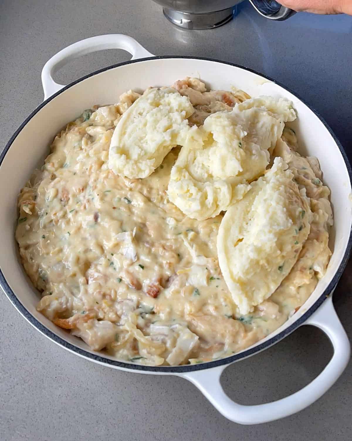 Smoked fish pie in a caseerole dish with mashed potato being spooned on top.